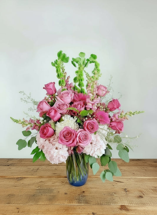 Bouquet of pink and white flowers in a clear vase on a wooden surface with a light gray background