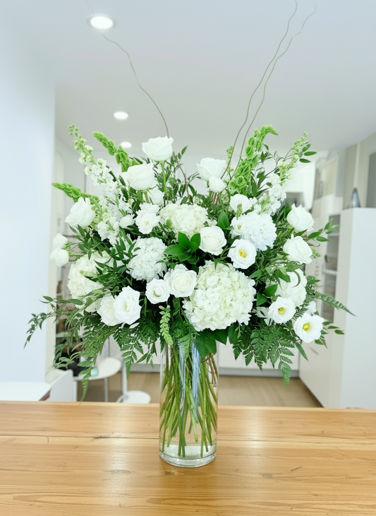 Bouquet of white flowers in a clear vase on a wooden table with a blurred indoor background