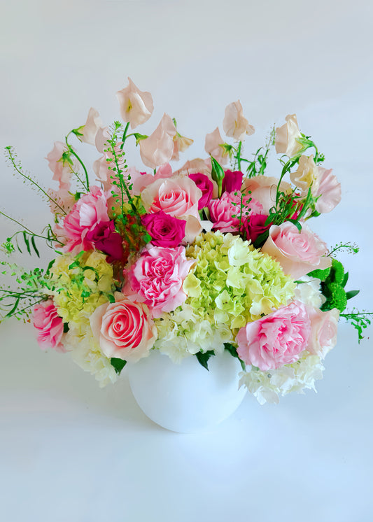 A floral arrangement featuring soft pink and white flowers with greenery in a white vase.
